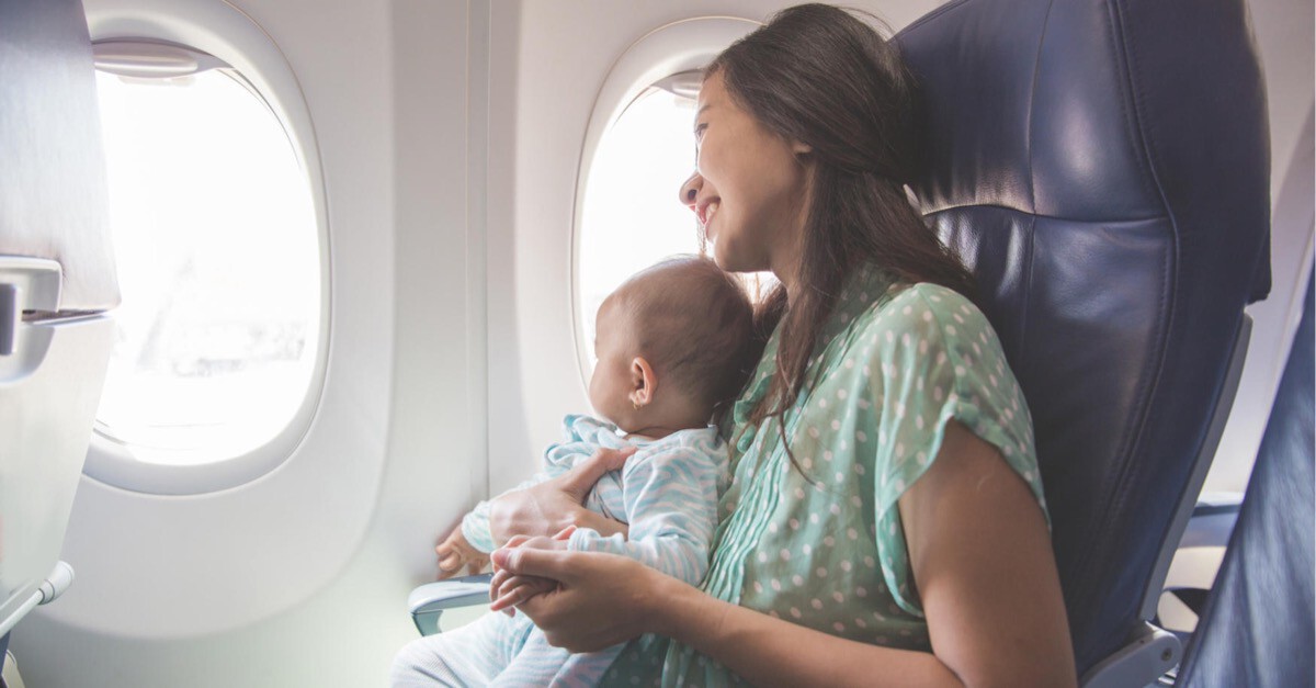 Baby sitzt am Schoß der Mutter und schaut aus Flugzeugfenster