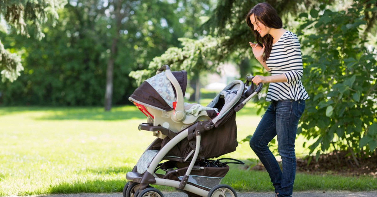 Frau spaziert mit Kinderwagen im Park