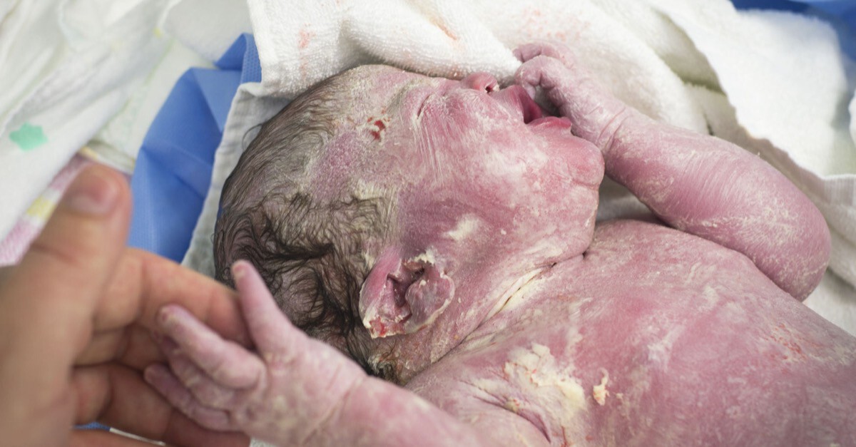 Vater hält Hand von Baby das von Käseschmiere bedeckt ist