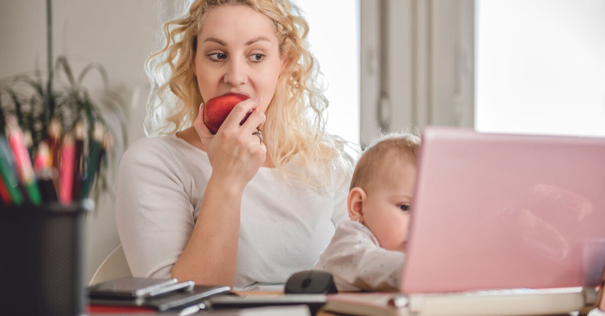 Mutter mit Baby isst Apfel vor Laptop