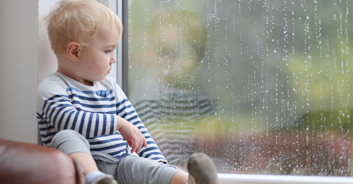 Kleinkind schaut aus Fenster bei regen